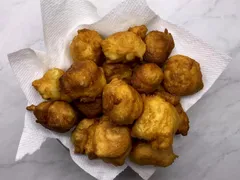 A bowl of golden-brown petulla on paper towel, on a marble counter
