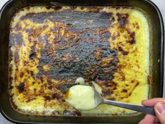 A spoonful of soft vanilla custard lifted from a tray of qumështor with a dark, broiled top